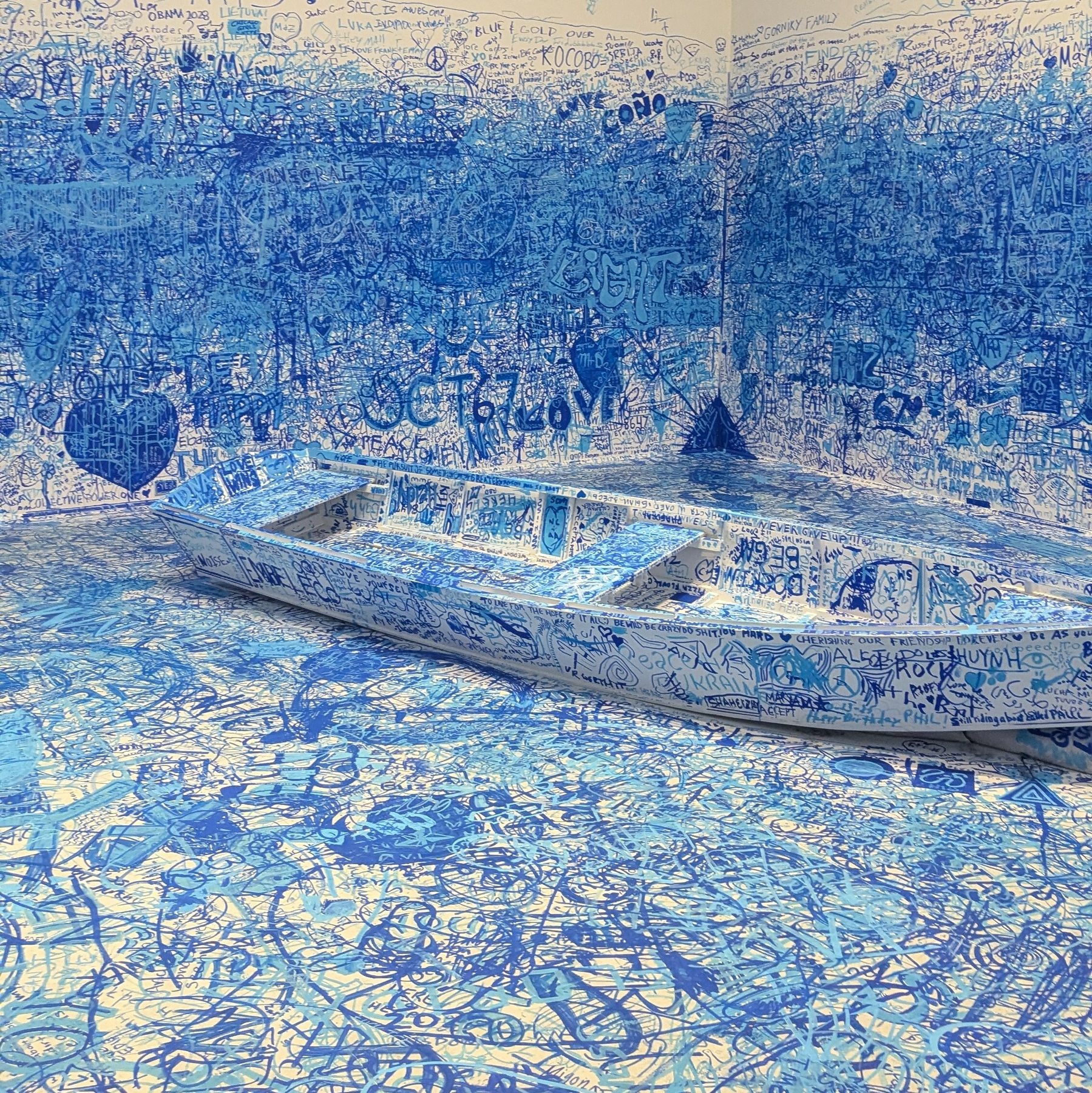 A room and a boat are covered in overlapping blue scribbles and drawings, creating a chaotic and immersive art installation.