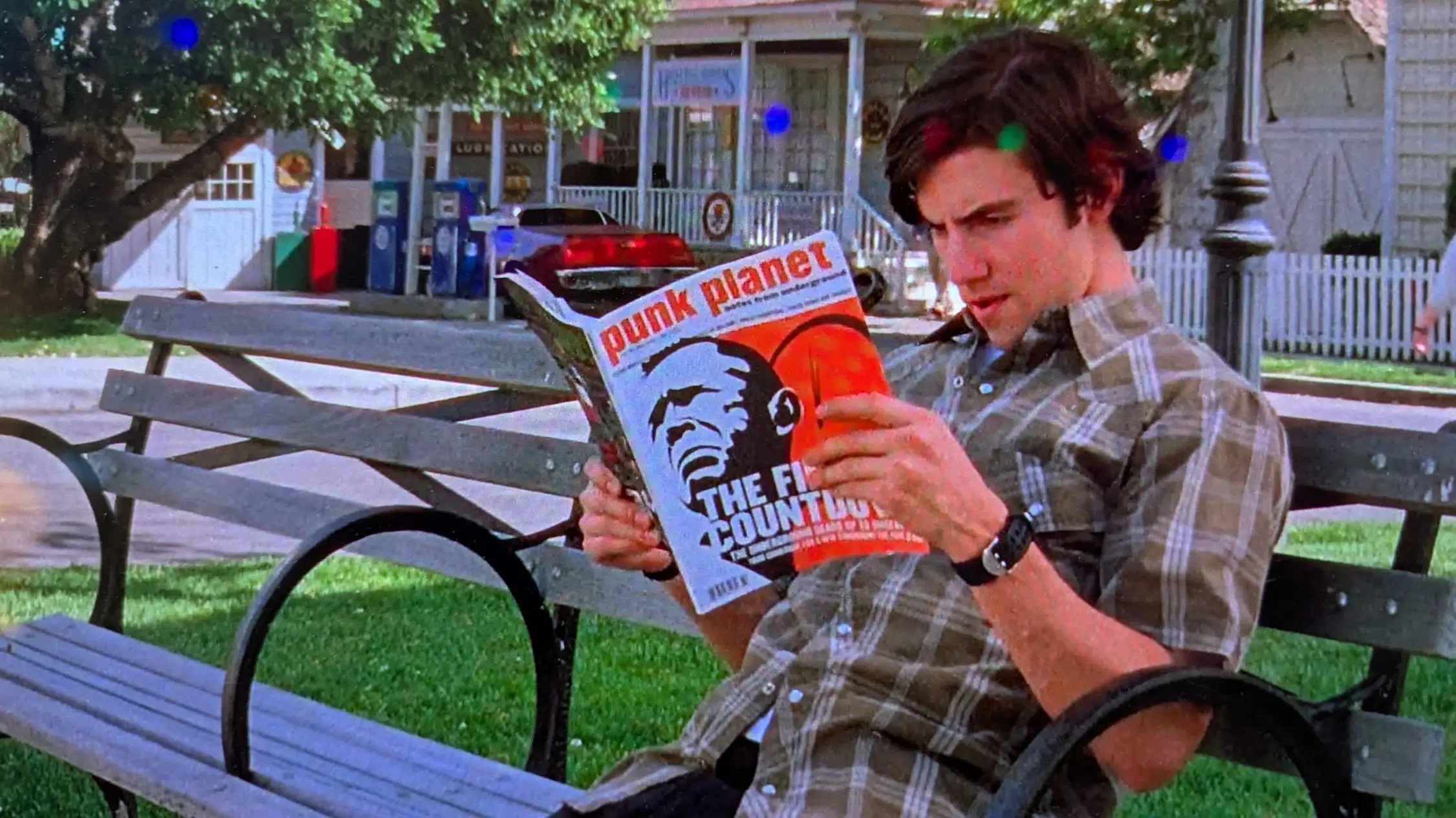 Jess, a character from the show the Gilmore Girls, reads a copy of  Punk Planet magazine on a park bench