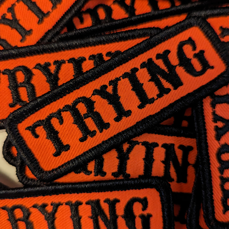 a pile of patches, orange with black type that reads 'trying'