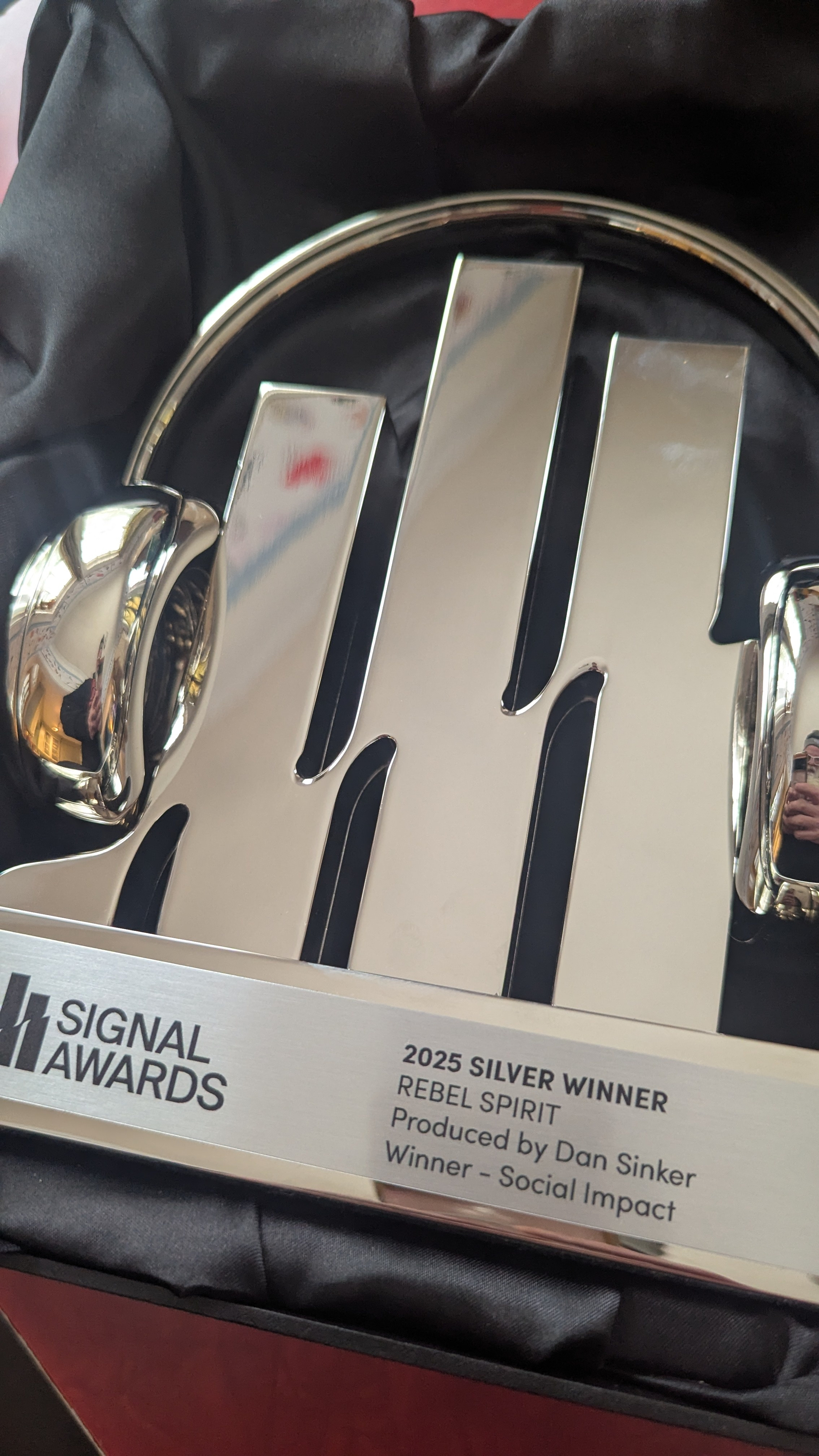 A silver award with the Signal Awards logo, titled 2025 Silver Winner for Rebel Spirit, produced by Dan Sinker in the Social Impact category, is displayed in a box.