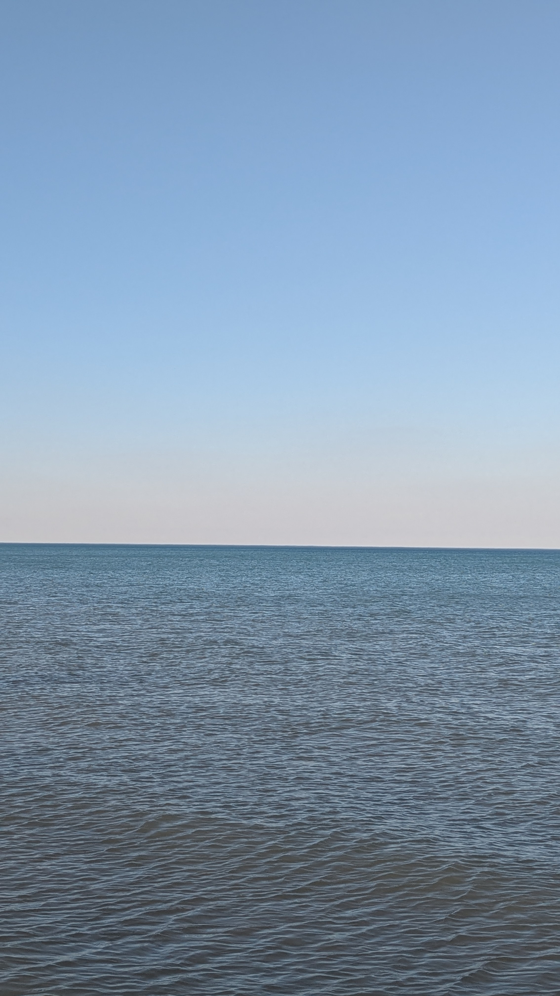 A calm lake michigan under a clear blue sky stretches towards the horizon.