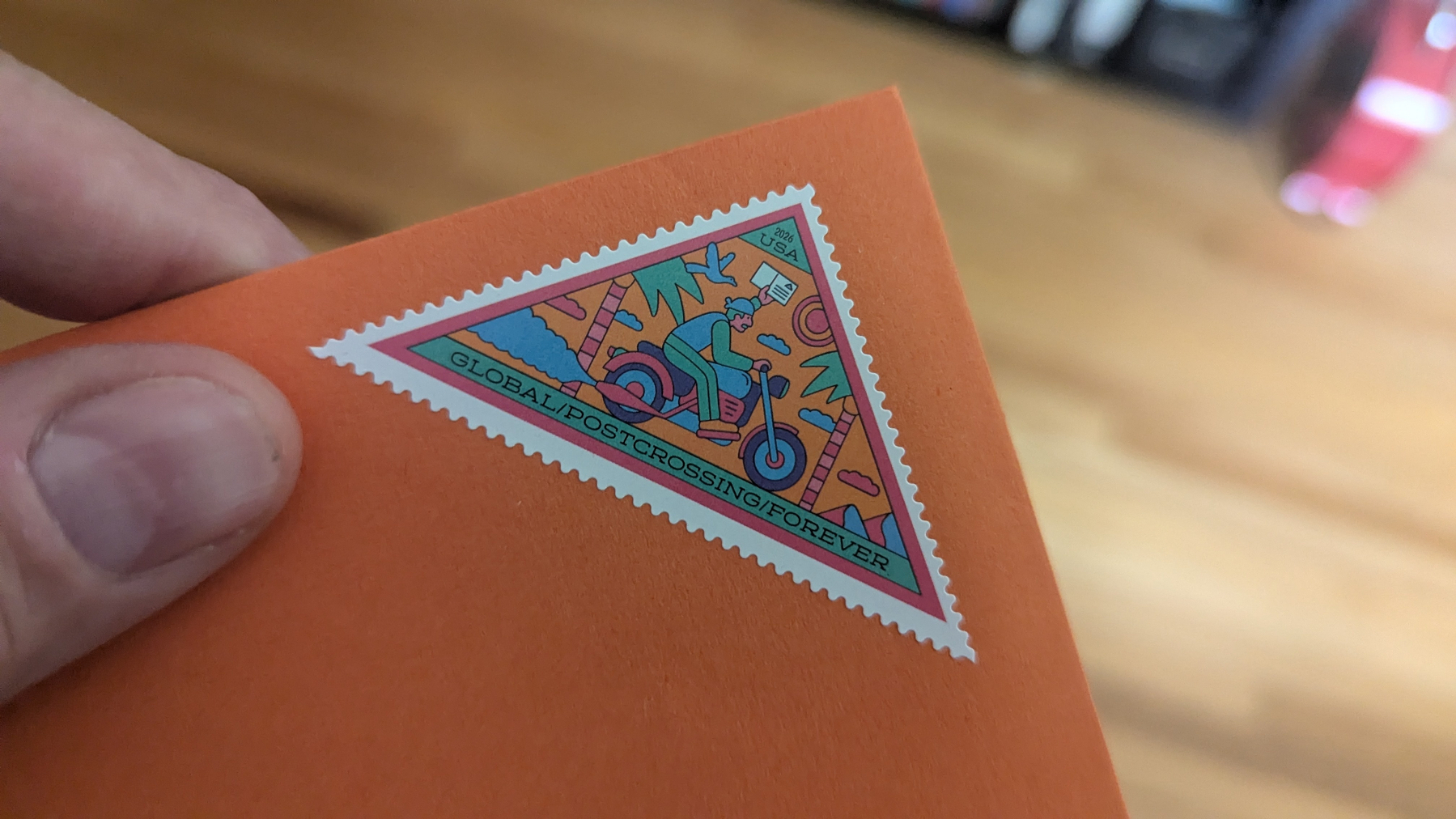 A hand holds an orange envelope with a colorful triangular stamp